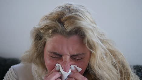 Close-up-of-a-sick-woman-sneezing-into-a-tissue
