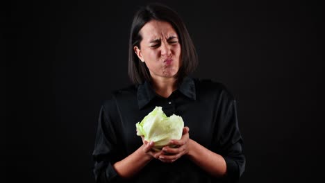 Young-Woman-Biting-Cabbage-With-Bad-Face-Expression,-Healthy-Vegan-Food-Concept,-Black-Backgrund