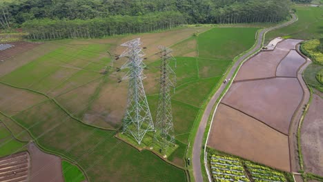 Aerial-drone-shot-over-high-voltage-electricity-tower-in-the-middle-of-rice-field---Indonesia,-Asia