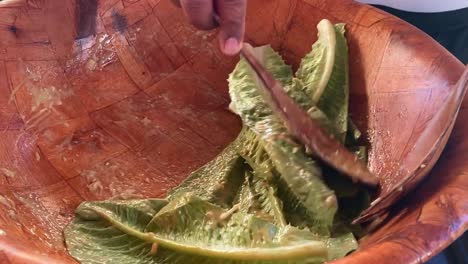 Close-up-of-lettuce-leaves-being-mixed-with-a-dressing-to-prepare-caesar-salad-in-a-bowl