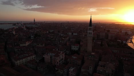 Sunset-in-Venice,-Italy,-Aerial-Drone-Above-Floating-City-of-Canals,-Golden-Sky-Sun-over-Buildings,-City-Town-Architecture-and-Campanile-Tower