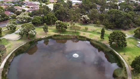 Aerial-Pull-Back-Shot-Over-Large-Circular-Lake-With-Established-Trees