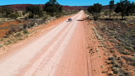 Cinematic-drone-video-from-car-driving-on-outback-road-in-red-sand-with-dust-australia
