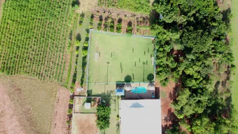 Overhead-Shot-Of-Summer-House-With-People-Playing-Soccer-In-Green-field