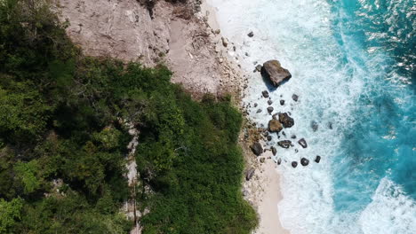 Cinematic-drone-video-from-beach-under-cliff-with-clear-blue-water-waves-and-white-sand