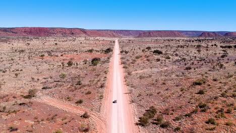 Filmisches-Drohnenvideo-Von-Einem-Auto,-Das-Auf-Einer-Outback-Straße-In-Rotem-Sand-Mit-Staub-Aus-Australien-Fährt