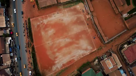 People-playing-street-football-on-a-red-clay-field-in-the-city-of-Africa---rotating,-high-angle,-drone-shot