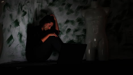 Depressive-Young-Woman-With-Tape-Over-Mouth-Reading-Bad-News-or-Hate-Messages-on-Laptop-in-Dark-Corner-of-Room