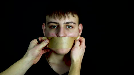 Person-Placing-Tape-Over-Mouth-of-Young-Man,-Slow-Motion