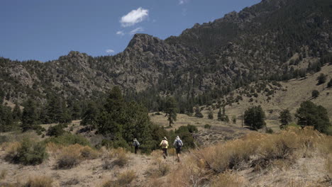 Hikers-walk-along-trail-in-Colorado-with-rugged-rocky-mountains-behind