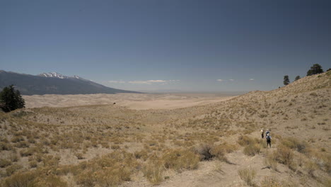 Hikers-walk-down-path-towards-Great-Sand-Dunes-National-Park-in-distance