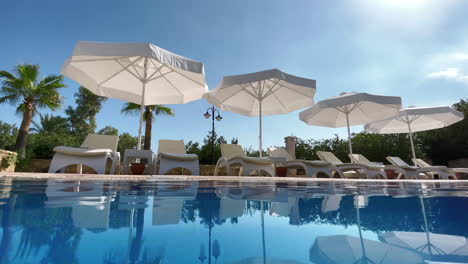 Lounge-chairs-with-parasols-beside-a-rippling-pool