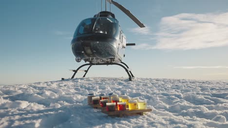 Helicopter-with-beer-in-foreground-on-top-of-a-snowy-mountain-range-in-Canada,-BC
