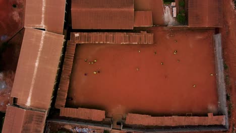 People-playing-street-soccer-on-a-red-sand-field-in-a-African-city--cenital,-aerial-view