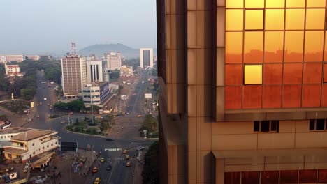 Ascending-aerial-view-close-to-a-reflecting-Block-number-2-building,-revealing-the-Ministry-district-of-Yaounde,-sunny-Cameroon