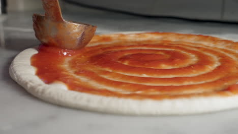 Salsa-De-Tomate-Esparcida-Sobre-La-Base-De-La-Pizza-En-Un-Movimiento-Giratorio,-Toma-De-Primer-Plano
