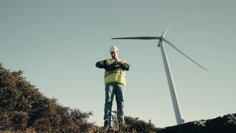 A-professional-Caucasian-engineer-in-a-reflective-vest-and-helmet-checks-wind-turbines-in-a-field,-showcasing-the-dedication-to-sustainable-energy-production