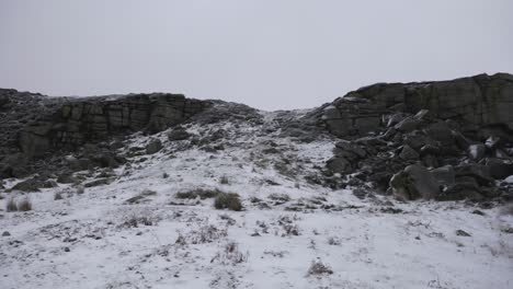 Two-men-hiking-through-snow-and-ice-in-front-of-a-fallen-rock-formation-in-winter