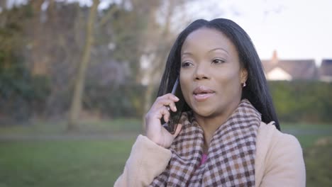 Confident-black-woman-talking-phone-in-park