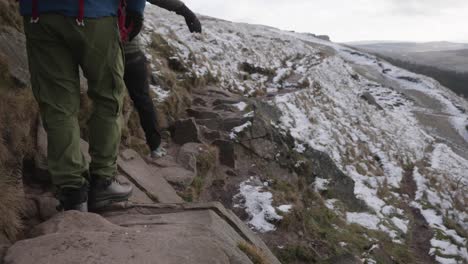 Two-men-hiking-and-scrambling-over-rocks-on-a-trail-in-frozen,-winter,-snowy-terrain