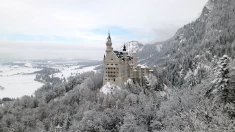 drone-flying-towards-neuschwanstein-castle-in-füssen-near-trees-in-winter