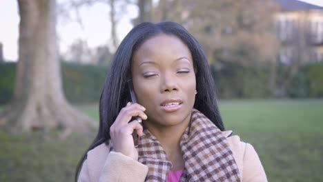 Confident-black-woman-talking-phone-in-park