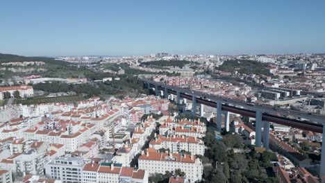 amazing-aerial-wide-drone-shoot-of-historic-old-town-of-Lisbon,-Alfama-in-Portugal-with-its-buildings-in-amazing-and-varied-pink-blue-and-yellow-colours-with-25-april-bridge-on-a-calm-sunny-day