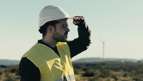 White-helmet-and-reflective-vest-clad-engineer-checks-wind-turbines-in-a-field-of-clean-energy-generators