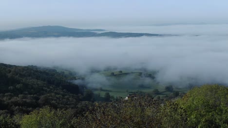 Drone-flying-over-forest-with-fog-shrouded-valley-in-background-on-sunny-day