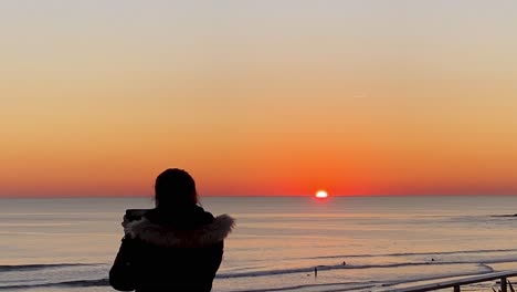 Silhouette-of-young-woman-takes-a-picture-from-phone-on-the-beach-at-huge-sunset
