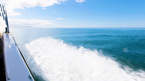 Boat-speeds-out-on-blue-open-ocean,-calm-surface---forward-facing-shot-over-side