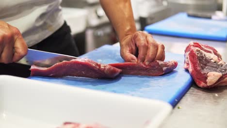 Close-up-of-a-chef-carefully-slicing-raw-sirloin-steak-with-knife-on-a-board-in-slow-motion