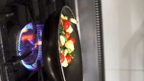 Vertical-close-up-clip-of-person-stirring-a-pan-of-vegetables-on-kitchen-stove-in-slow-motion