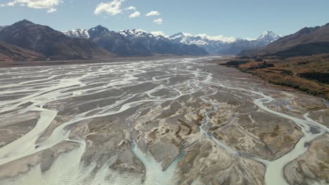 Panoramic-aerial-arc-above-river-delta-showing-striking-textures,-snowy-Aoraki-Mount-Cook-mountains-in-background