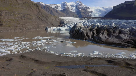 Aerial:-Backwards-reveal-shot-of-one-man-standing-still-on-a-hill-near-Svinafellsjokull-glacier-during-a-sunny-day
