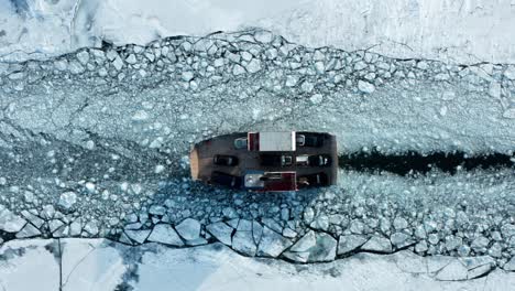 Car-ferry-transporting-vehicles-through-broken-frozen-lake-ice-sheet-path,-aerial-top-down