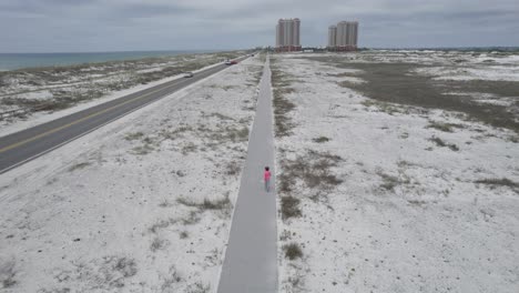 Mujer-Caminando-Por-El-Carril-Bici-De-La-Playa-Vestida-De-Rosa-Haciendo-Ejercicio-En-El-Golfo-De-México