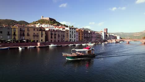 Aerial-tracking-of-tourist-boat-cruise-on-canal-with-colored-medieval-town-in-background