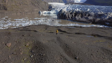 Aerial:-Slow-panning-shot-of-one-man-standing-on-a-hill-near-Svinafellsjokull-glacier-during-a-sunny-day