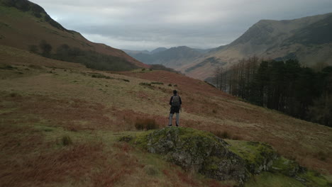 Flying-past-hiker-on-rocky-outcrop-towards-distant-misty-mountains-at-Buttermere-English-Lake-District-UK