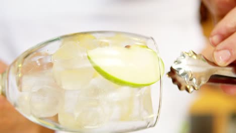 Vertical-close-up-of-a-person-leaving-in-slow-motion-a-piece-of-apple-inside-a-glass-with-ice-cubes