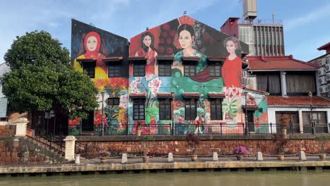 Beautiful-frontal-view-of-murals-and-people-strolling-along-the-Malacca-River-Waterfront,-a-famous-tourist-spot-in-Malacca,-Malaysia