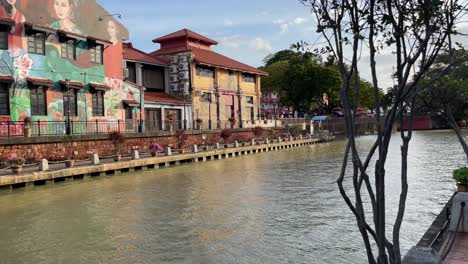 Schwenkblick-Auf-Die-Wunderschönen-Wandgemälde-Und-Touristen,-Die-Die-Entspannte-Atmosphäre-Am-Flussufercafé-Genießen,-Einem-Berühmten-Touristenort-In-Malakka,-Malaysia