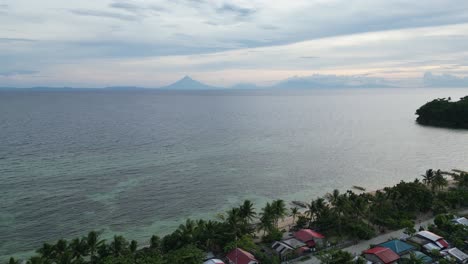Aerial,-Establishing-Drone-Shot-of-Breathtaking-Beach-and-quaint-barangay-with-silhouette-of-Mayon-Volcano-in-background-during-dusk,-Catanduanes,-Philippines