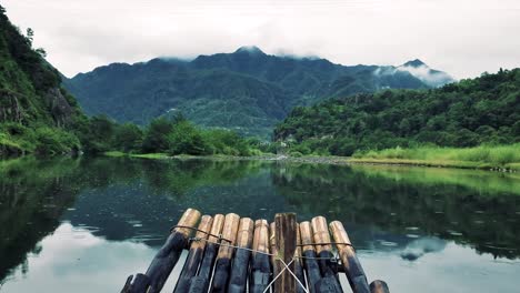 POV-of-a-raft-made-of-branches-sailing-on-a-lake-with-green-mountains-in-the-background-in-a-heavenly-place-in-the-middle-of-nowhere