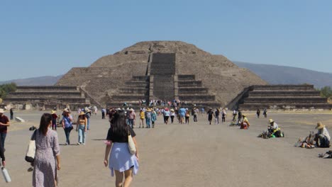 A-hyper-lapse-dolly-in-shot-of-tourists-walking-towards-the-Pyramid-of-the-Moon-in-the-archaeological-zone-of-Teotihuacan,-Mexico,-on-a-wide-road-with-many-people,-on-a-clear-and-sunny-day