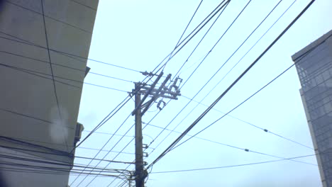 look-up-slight-movement-view-of-an-old-vintage-simple-electricity-pole-with-complicated-cable-lines-across-hanging-in-the-sky-horizontal-and-vertical-onto-the-apartment-building-in-cloudy-gloomy-day