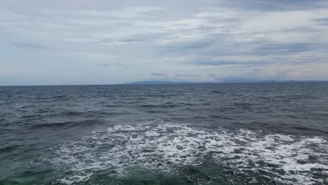 Luftdrohnenaufnahme-Von-Schäumenden-Wellen,-Die-Mitten-Im-Riesigen-Ozean-Auf-Ein-Riff-Krachen,-Mit-Bewölktem-Himmel-Im-Hintergrund