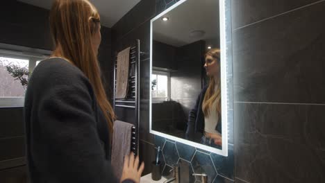 Weibliches-Model-Schaut-In-Einen-Badezimmerspiegel-Mit-Hintergrundbeleuchtung-Und-Sortiert-Ihre-Haare