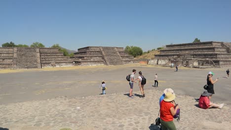 Slow-motion-panning-shot-of-the-archaeological-site-of-Teotihuacan-in-Mexico,-with-the-Pyramid-of-the-Moon-in-the-center-and-tourists-walking-around-on-a-clear-and-sunny-day
